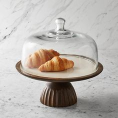 two croissants under a glass clochet on a plate with marble background