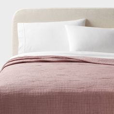 a bed with pink sheets and white pillows on top of it, next to a beige headboard