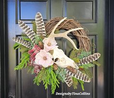 a wreath with antlers, flowers and feathers is hanging on the front door doors