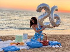 a woman sitting on the beach with her 30th birthday cake and balloons in front of her