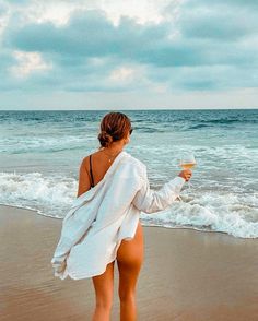 a woman standing on top of a beach next to the ocean holding an ice cream cone