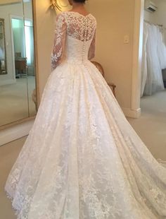 a woman in a white wedding dress looking at herself in the mirror with her back to the camera