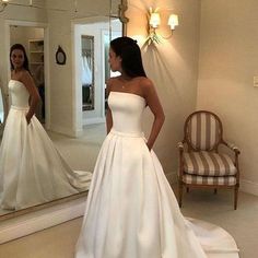 a woman standing in front of a mirror wearing a white wedding dress and looking at her reflection