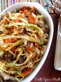 a white bowl filled with cabbage and meat on top of a table next to silverware