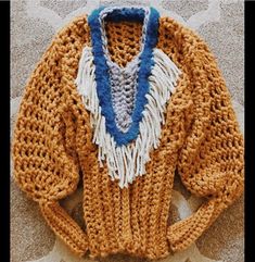 a crocheted sweater with blue and white trims on the front, sitting on a carpet