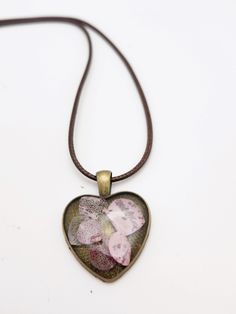 a heart shaped pendant with pink flowers on a brown leather cord hanging from a white background