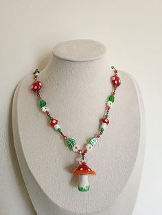 a necklace on a mannequin is decorated with beads and charms, including an orange mushroom