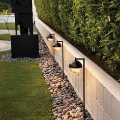 some lights that are sitting on the side of a wall next to grass and bushes