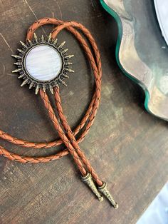 This awesome bolo tie has a southwestern brass sun design and pearl white stone centerpiece. The cord is brown genuine leather. Our bolos pair nicely with many of our belt buckles! They make wonderful gifts. The western bolo tie rope length is 39'' ; charm pendant size is 1 1/2'' Western Bolo Tie, Sun Design, Wire Ring, Sun Designs, Bolo Tie, Wire Rings, You Are My Sunshine, White Stone, Fall Outfits Women