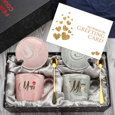 two matching mugs in a gift box with gold spoons and a greeting card