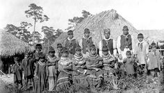 a group of people standing next to each other in front of a thatched hut