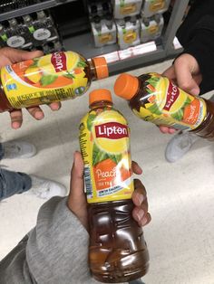 three people holding up two bottles of lipton orange juice