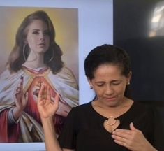 a woman standing in front of a painting holding her hand up to the side with both hands