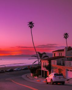 a car parked on the side of a road next to a palm tree at sunset