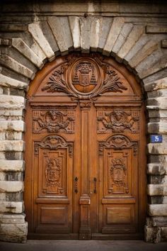 two wooden doors with carvings on them in front of a brick wall and stone arch