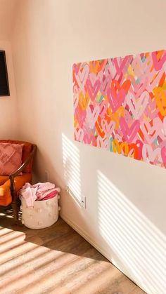 an orange chair sitting in front of a painting on the wall next to a window