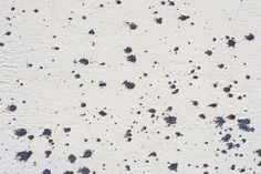 black and white paint splattered on the side of a concrete wall with small holes in it