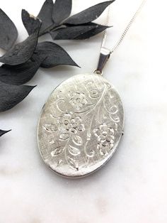 A Lovely Large Vintage Sterling Silver Oval Locket.  Beautifully hand engraved flowers on the front with a textured finish on the back.  It is stamped on the top bail SILVER.  The locket is in perfect working condition, it opens and closes perfectly and securely.  Inside the locket it has both original frames for your photos.  The locket measures 2.2 inches including the top bail.  It's on a new Sterling Silver 18 inch curb chain. Engraved Flower Pendant Necklace For Keepsake, Antique Silver Engraved Flower Pendant Necklace, Antique Silver Flower Pendant Necklace With Engravings, Vintage Silver Flower Pendant Locket Necklace, Ornate Medallion Jewelry, Ornate Medallion Stamped Jewelry, Antique Silver Engraved Flower Pendant Jewelry, Elegant Etched Oval Pendant Locket Necklace, Vintage Engraved Flower Pendant Jewelry