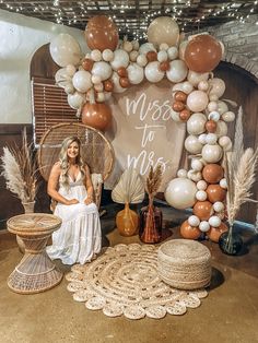 a woman sitting on a chair in front of a balloon arch