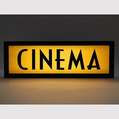 an illuminated sign that says cinema in black and yellow colors on a gray background with the word'cinema'below it