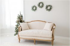 a white couch sitting next to a christmas tree in front of two wreaths on the wall