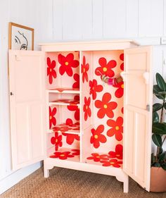 a cabinet with red flowers painted on the doors and drawers is next to a potted plant