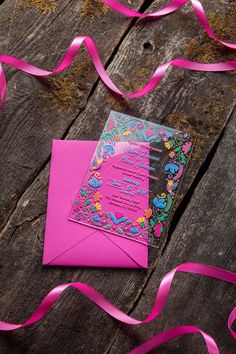 a pink envelope and ribbon on top of a wooden table