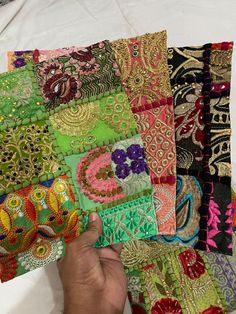 a person is holding up several pieces of colorful fabric on a white table cloth, which has been stitched together