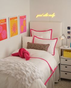 a white bed with pink and yellow pillows on top of it next to a night stand