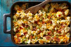 a casserole dish with bacon, cheese and green onions in it next to a wooden spoon