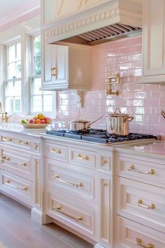 a large kitchen with white cabinets and pink tile backsplash, gold handles on the stove