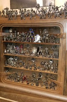 a display case filled with metal figurines on top of wooden shelves next to a painting