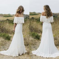 a woman in a white wedding dress standing on a dirt road with her back to the camera