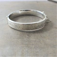 A beautifully engraved scrollwork graces this bangle on the front; the back is without decoration.  The bracelet, made in Chester, England in 1960, is fully hallmarked on the interior with the English standard for sterling.  The lovely piece opens with and closes with a click, it has a safety chain for added security.Bracelet (closed):approx.  2 1/4 x 2 1/16"width 7/16" (14m)interior perimeter 6 3/4"BB005✦All of our vintage bracelets ship with complimentary insurance✦✤Our entire selection of bra Victorian Style Engraved Silver Bangle, Victorian Style Silver Engraved Bangle, Victorian Silver Engraved Bangle, Victorian Etched Cuff Bracelet, Ornate Stamped Bracelets For Formal Occasions, Victorian Etched Cuff Bracelet For Wedding, Formal Engraved Bangle Cuff Bracelet, Victorian Sterling Silver Engraved Wedding Bracelet, Victorian Engraved Cuff Bracelet For Anniversary