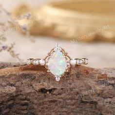 an opal and diamond ring sitting on top of a piece of wood with flowers in the background