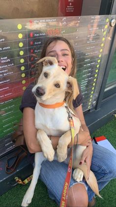 a woman sitting on the ground holding a dog in her lap and smiling at the camera