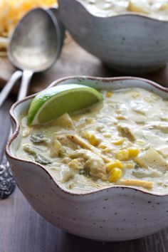 a white bowl filled with chicken and corn soup next to a spoon on a wooden table