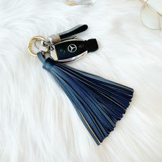 a key chain with a blue tassel and mercedes logo on it sitting on a white fur surface