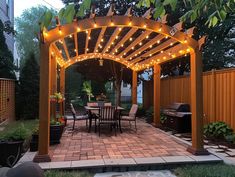 an outdoor patio with lights on the pergolated area and grill in the background