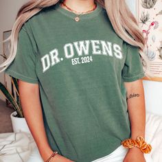 a woman with long blonde hair wearing a green dr owens t - shirt