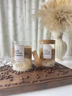 two candles sitting on top of a wooden table next to coffee beans and a vase