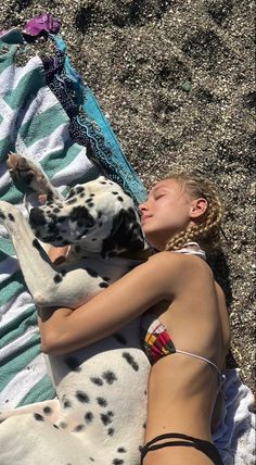 a woman laying on top of a towel next to a dalmatian in the sand