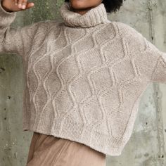 a woman wearing a turtle neck sweater and tan pants with her hands in the air