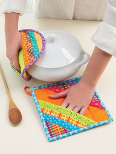 a woman is using a pot holder on top of a cloth with a wooden spoon next to it