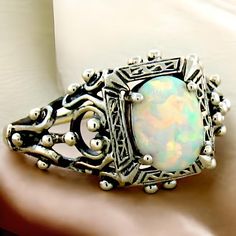 Introducing a stunning piece of history and craftsmanship: our Vintage Estate Lab Created Cabochon Opal Solitaire Filigree Ring. This exquisite ring is meticulously crafted from solid 925 sterling silver, showcasing the timeless beauty of filigree work that adds intricate elegance to any outfit. The centerpiece of this enchanting ring is a high-quality lab created opal stone, measuring 8x6 mm, which radiates hues of mesmerizing blue and green, mirroring the shimmering depths of the ocean. With the top of the ring measuring nearly 1/2 inch in length, it's a standout piece that draws admiration without being overwhelming. Not only does this ring embody vintage glamour, but it also represents a commitment to sustainability. This stunning ring is stamped with "925," ensuring you receive authen Classic Opal Ring Collectible, Vintage Hallmarked Opal Ring For Anniversary, Vintage Opal Gemstone Ring For Wedding, Vintage Opal Ring For Wedding, Vintage Style Opal Wedding Ring, Heirloom Style Opal Ring Gift, Heirloom White Jewelry For Ceremonial Occasion, Victorian Cabochon Opal Ring For Gift, Vintage Silver Opal Cabochon Ring