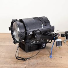 a projector sitting on top of a wooden table next to some wires and plugs