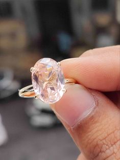 a woman's hand holding an engagement ring with a large pink diamond in it