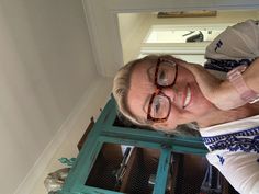 an older man wearing glasses standing in front of a blue window with glass panes