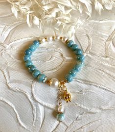 a bracelet with blue beads and gold accents on a white fabric covered tablecloth next to a flower