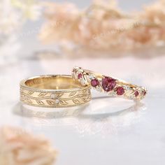 two gold wedding bands with red and white stones on them, sitting next to each other